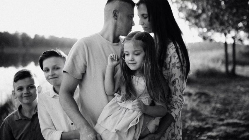 A serene black and white portrait of a family standing by a lake.